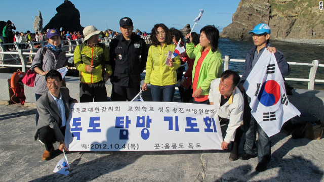 A group of tourists from South Korea arrives on the islands on a ferry carrying flags. Kevin Kim, 40, says, "I'm a native of Korea and an American citizen but in my blood I'm Korean... I feel so great to be here... It really makes me upset when Japan claims this island, it's absurd and it should not be tolerated."