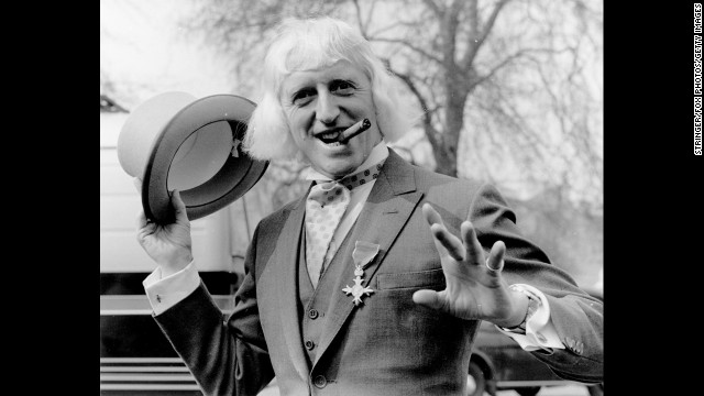 British radio disc jockey, television star and charity fund-raiser Sir Jimmy Savile poses for a photo at Buckingham Palace, London, after receiving the Order of the British Empire in 1972. Since his death a year ago at age 84, Savile has been knocked off his perch as a national treasure, accused of being a predatory pedophile who used his fame and position to abuse youngsters, sometimes on BBC premises.