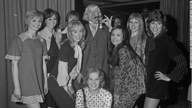 Savile shows off his Order of the British Empire to members of the "Second Generation" song and dance troupe.