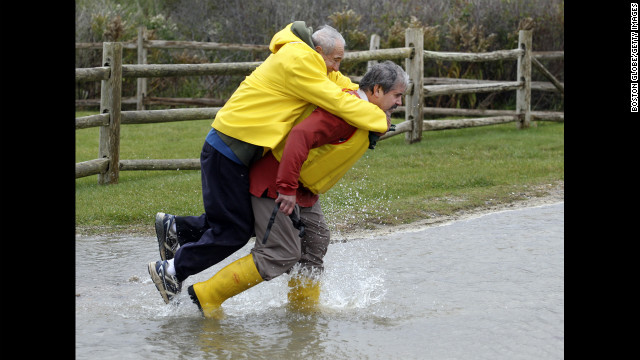 Chris Losordo carries his father, Vin, across a flooded road in Falmouth, Massachusetts, on Monday.