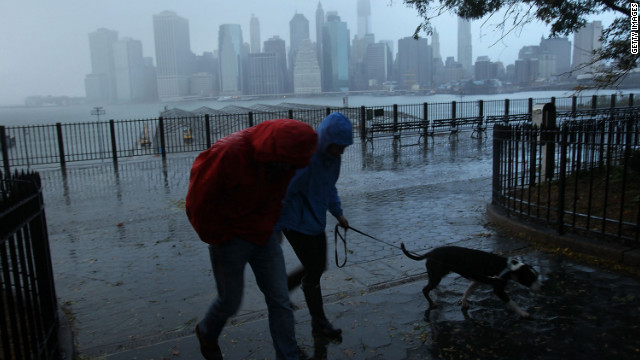 A couple walks in the rain Tuesday, with the East River and the Lower Manhattan skyline as a backdrop.