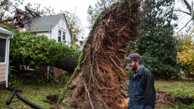 Sam Rigby walks on Tuesday near an uprooted tree that grazed his house and hit his neighbor's house in Washington.