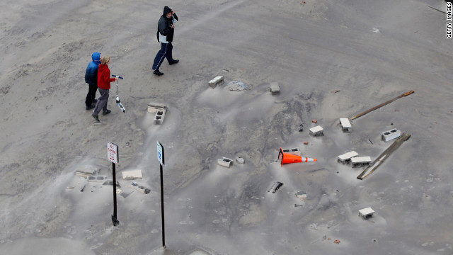 Residents walk along a street covered in beach sand after floodwaters from Superstorm Sandy retreated Tuesday in Long Beach.