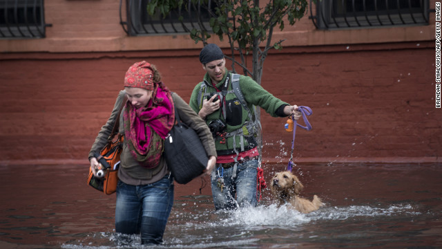 Blaine Badick and her fiancee Andrew Grapsas cross a flooded street with their dog while leaving their home in Hoboken.