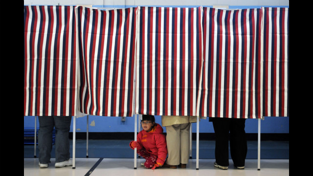 A young girl peers out from under a voting booth as her mother casts a ballot at the Bishop Leo O'Neil Youth Center in Manchester, New Hampshire. 