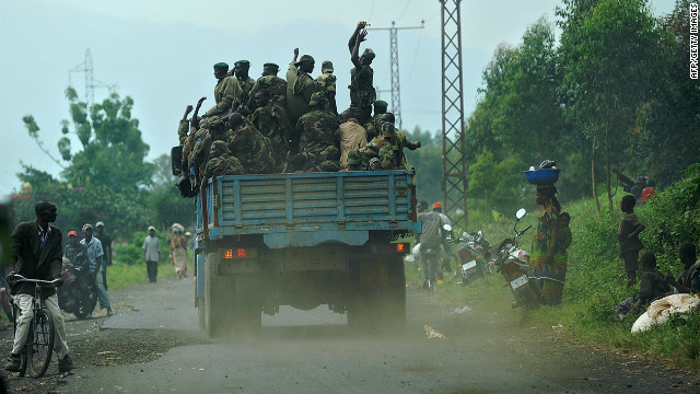 Fighters from the M23 rebel movement ride on the back of a truck, passing a camp for the internally displaced in Mugunga, Democratic Republic of Congo on November 24, 2012.