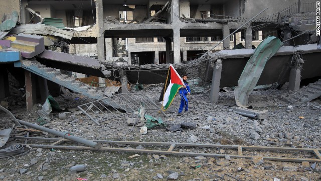 A Palestinian boy carries the national flag as he makes his way through the debris of the destroyed Palestine Stadium.