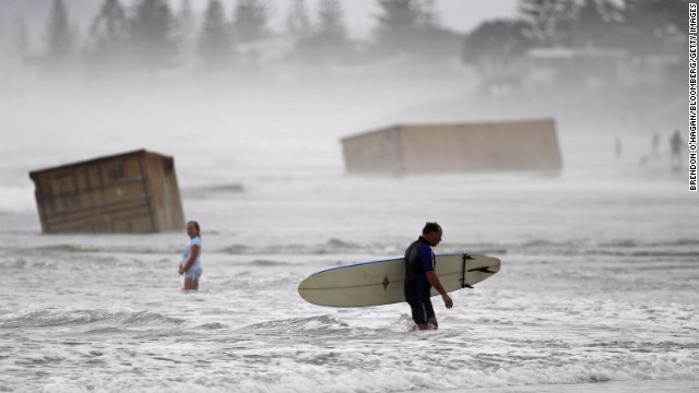 January 10: A surfer walks past cargo containers washed ashore from the stricken container ship Rena at Waihi Beach in New Zealand. The ship was stranded on a reef for more than three months before breaking up and sinking in rough seas, littering beaches with cargo and debris.