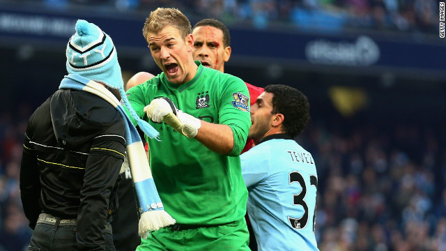 Manchester City goalkeeper Joe Hart of confronts a pitch invader at the end of his side's 3-2 derby defeat by Manchester United, whose defender Rio Ferdinand (at back) was left with a bloody face after being hit by a coin thrown from the crowd. 