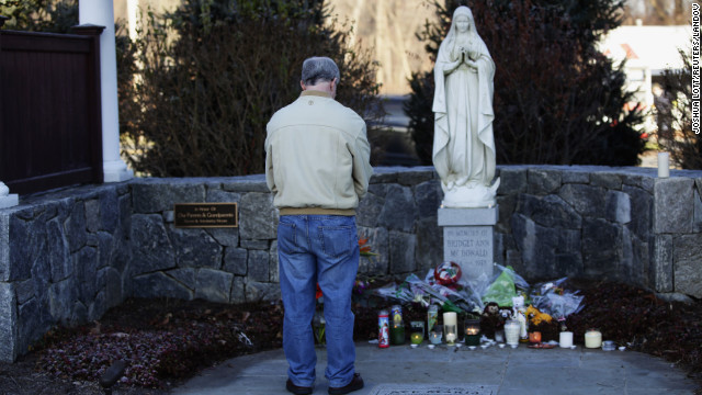 A man bows his head as he stands at a makeshift memorial, outside Saint Rose of Lima Roman Catholic Church in Newtown on Saturday, December 15.