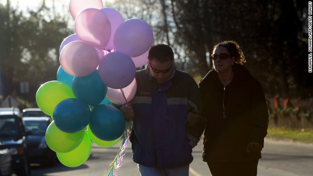 A couple carry balloons to place at a curbside shrine to in Newtown on Saturday.