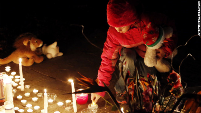 A child lights a candle at a memorial filled with flowers, stuffed toys and candles outside of Saint Rose of Lima Church near Sandy Hook Elementary School in Newtown, Connecticut on Saturday.