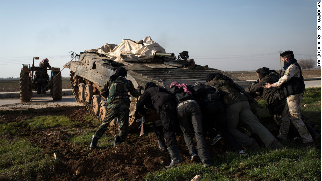 Rebel fighters push an abandoned Syrian army tank with the aid of a tractor in Aleppo on January 18. The tank is to be repaired and used by rebels. 