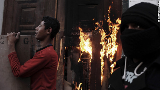 Egyptian protesters stand by the burning door of a school building on January 26, in Cairo.