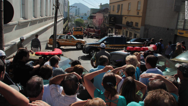 Residents look on as bodies of victims are transferred from the site of the fire to a municipal sports center.