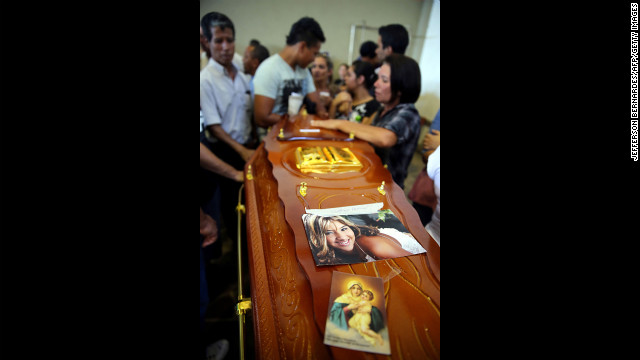 A coffin decorated with a photograph and image of the Virgin Mary is surrounded by mourners.