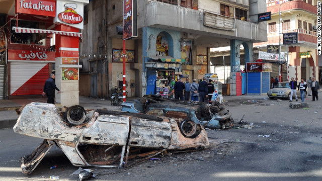 Egyptians walk past destroyed cars in Port Said on January 28 following the funeral of those killed in clashes.