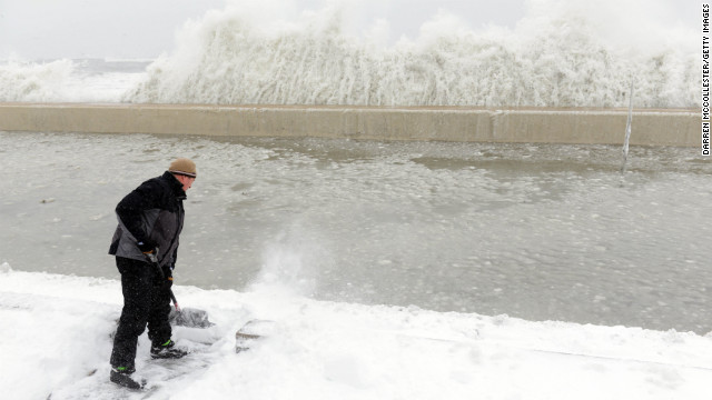 Mike Streeter shovels snow in his front yard as ocean water crashes over the sea wall just feet away on February 9 in Winthrop, Massachusetts.