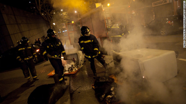 Firemen extinguish a bin on fire during a riot after a march by thousands of people.