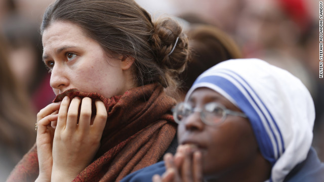 People watch a giant screen showing the departure of Pope Benedict XVI from Vatican City.