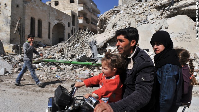 A Syrian man and his family drive past damaged buildings in Maarat al-Numan, on Wednesday, March 20.