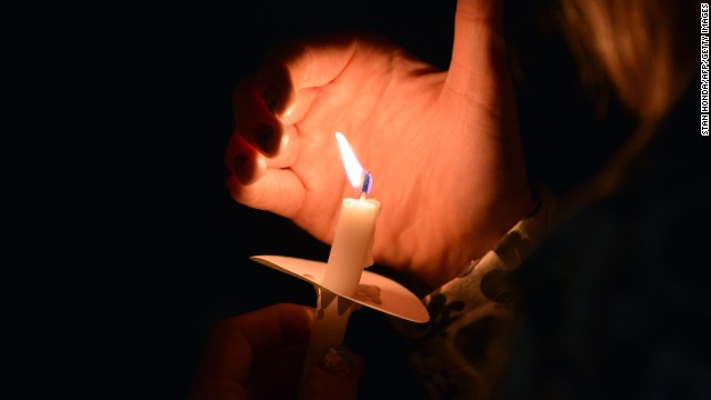 A woman uses her hand to keep wind from her candle as she stands with others around the pond in the Boston Public Gardens after a candlelight interfaith service at Arlington Street Church on April 16.