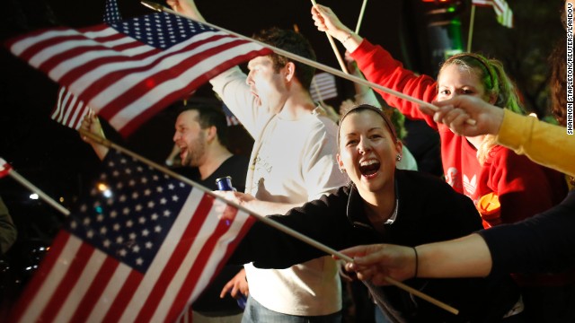 People wave U.S. flags as police drive down the street on April 19.