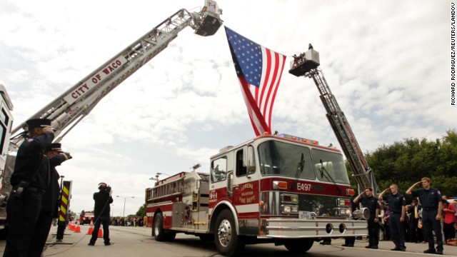 Firefighters salute as fire trucks and emergency vehicles pass under a flag before the memorial service on April 25.