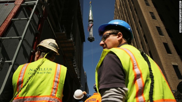 Construction workers watch as the 408-foot spire is hoisted onto a temporary platform on the top of One World Trade Center. 