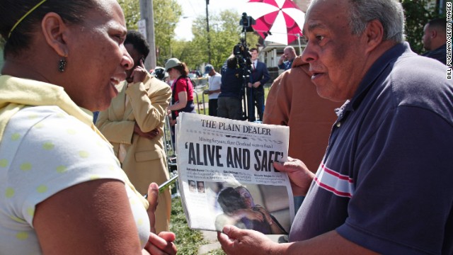A bystander shows the front page of The Plain Dealer newspaper to a friend outside of the house on Seymour Avenue on May 7.