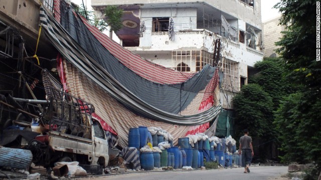 A man walks past a wall of barrels and linens on Wednesday, May 29, erected in Homs to provide protection from snipers.