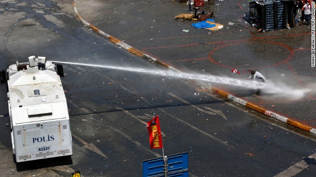 Riot police aim a water cannon at a protester as others take cover behind a makeshift shelter in Taksim Square on June 11.