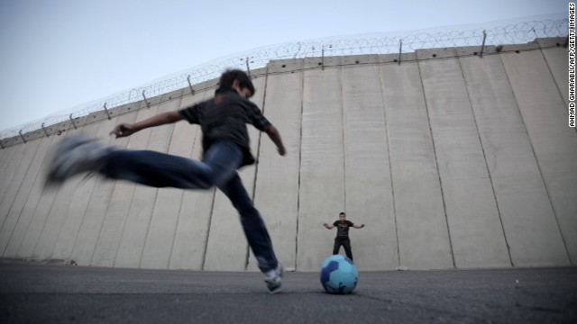 Palestinian children play football in front of the Israeli security fence in the West Bank village of Abu Dis, on the outskirts of Jerusalem. Organizations such as Mifalot help bring Palestinian and Israeli kids together through the power of football.