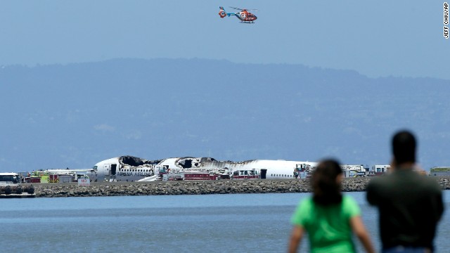 A helicopter flies above the wreckage on July 6 as people observe from across the waters of San Francisco Bay.