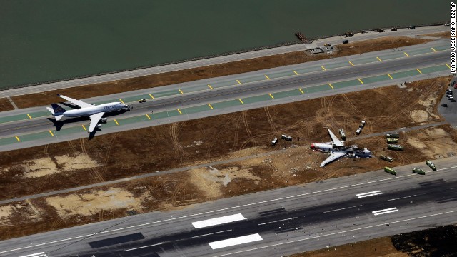 A plane sits on the runway on July 6 while emergency crews tend to the crash site.