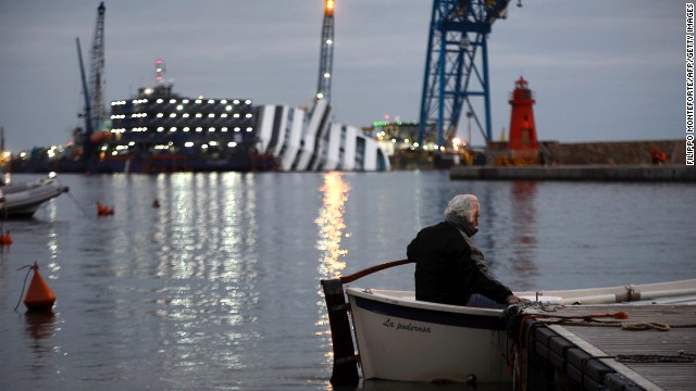 A man sits in his boat in front of the half-submerged cruise ship on January 8, 2013.