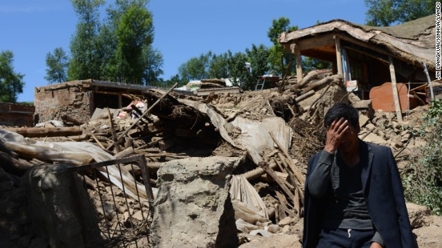 A man sits beside a collapsed house in Gansu province, in northwest China, on July 23.