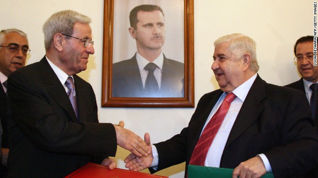 Syrian Foreign Minister Walid Muallem, right, and his Lebanese counterpart, Fawzi Salloukh, shake hands under a portrait of al-Assad in Damascus on October 15, 2008, after signing an agreement to restore diplomatic relations.