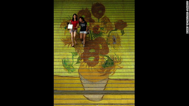 Shoppers walk down stairs featuring a reproduction of van Gogh's "Sunflowers" at the entrance to Ocean Terminal in Hong Kong.