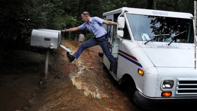 Dave Jackson closes a mailbox with his foot after delivering the mail to a home surrounded by water from the flooded Cheyenne Creek in Colorado Springs, Colorado, on Friday, September 13. Flooding in Colorado has washed away roads and bridges and flooded homes. Authorities warned more rain was on the way, threatening more flooding. At least four people have been killed and 218 are unaccounted for, officials say.