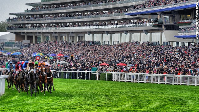 Royal Ascot, Ascot, Berkshire, UK: A packed grandstand watches a tightly-bunched group of runners during a race at Royal Ascot in June. 