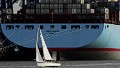 A yacht sails behind a giant Maersk cargo ship at the port of Felixstowe, England.