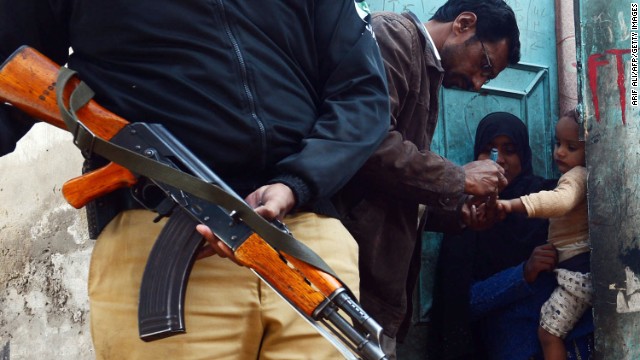 Efforts to stamp out the crippling disease have been hampered by resistance from the Taliban, who have banned vaccination teams from some areas. A Pakistani policeman stands guard as a polio vaccination worker marks a child after immunization with anti-polio drops an infant in Lahore on December 21, 2012.