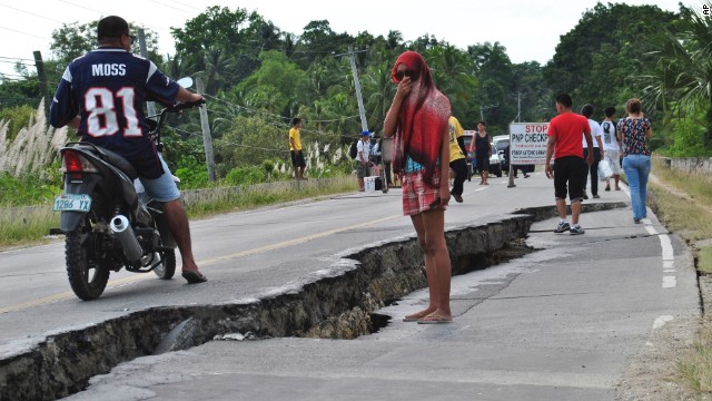 People walk along a damaged road in the province of Bohol on Tuesday, October 15.