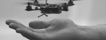 A quadrotor flying robot hovers above a man's hand