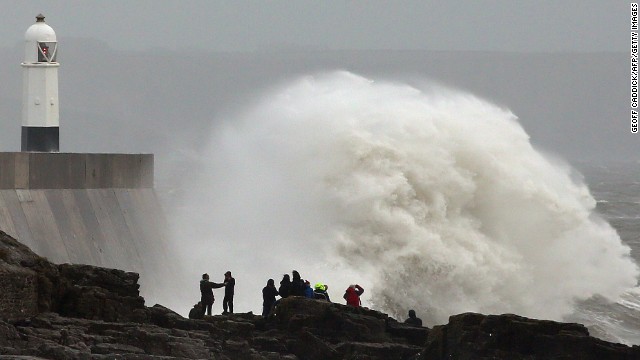 People stand on the rocks as large waves break against the harbor in Porthcawl, Wales, on Sunday.