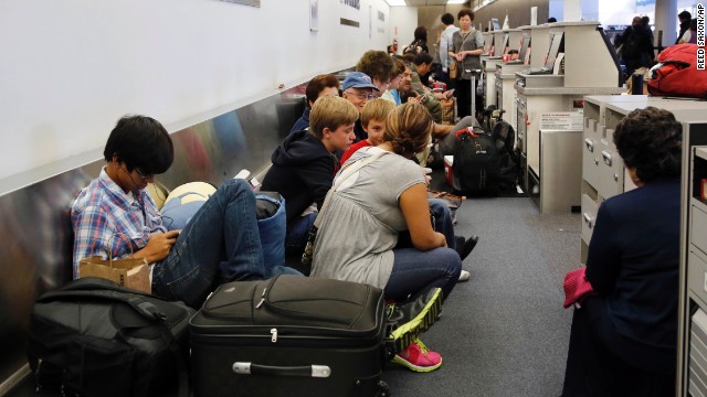 Passengers sit on a luggage conveyor belt behind check-in kiosks in Terminal 1.