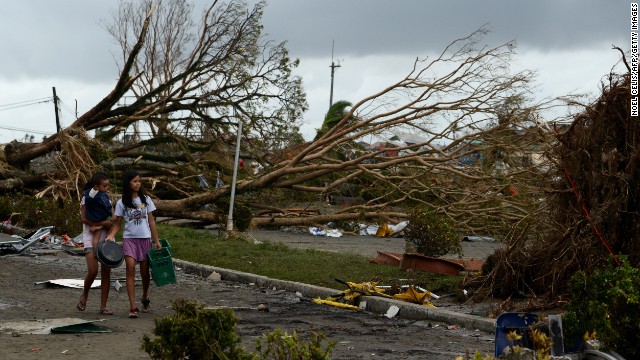 Women walk past fallen trees and destroyed houses in Tacloban on November 9. Residents scoured supermarkets for water and food as they slowly emerged on streets littered with debris.