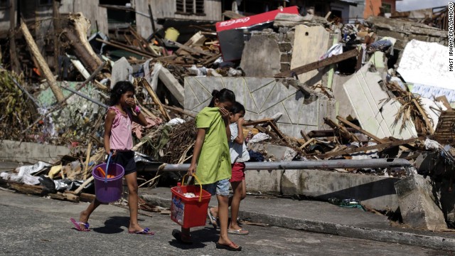 Children carry relief goods as they pass by damaged houses in Tacloban on November 13. 