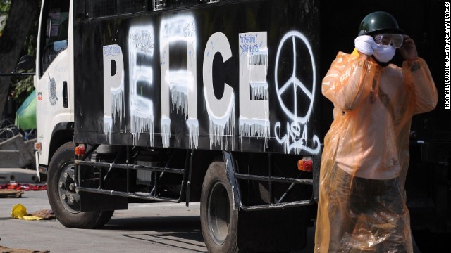 An anti-government protester walks past a police vehicle with the word "peace" painted where "police" used to be.